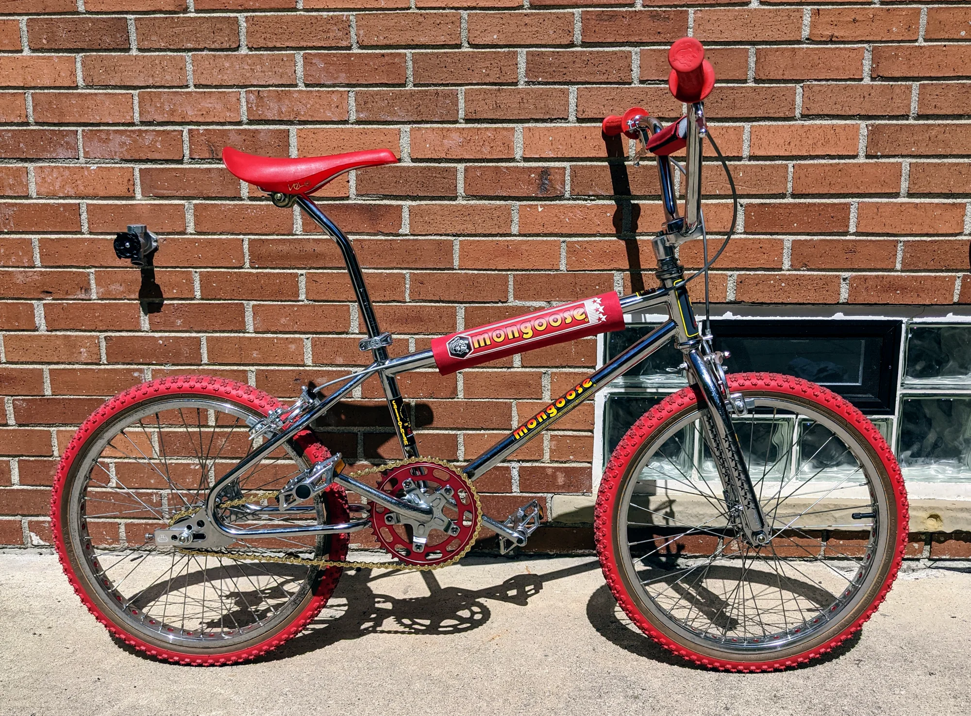 Side profile of a 1983 Mongoose Californian with a dark frame, chrome components, and red tires, saddle, grips, pads, and chainring.