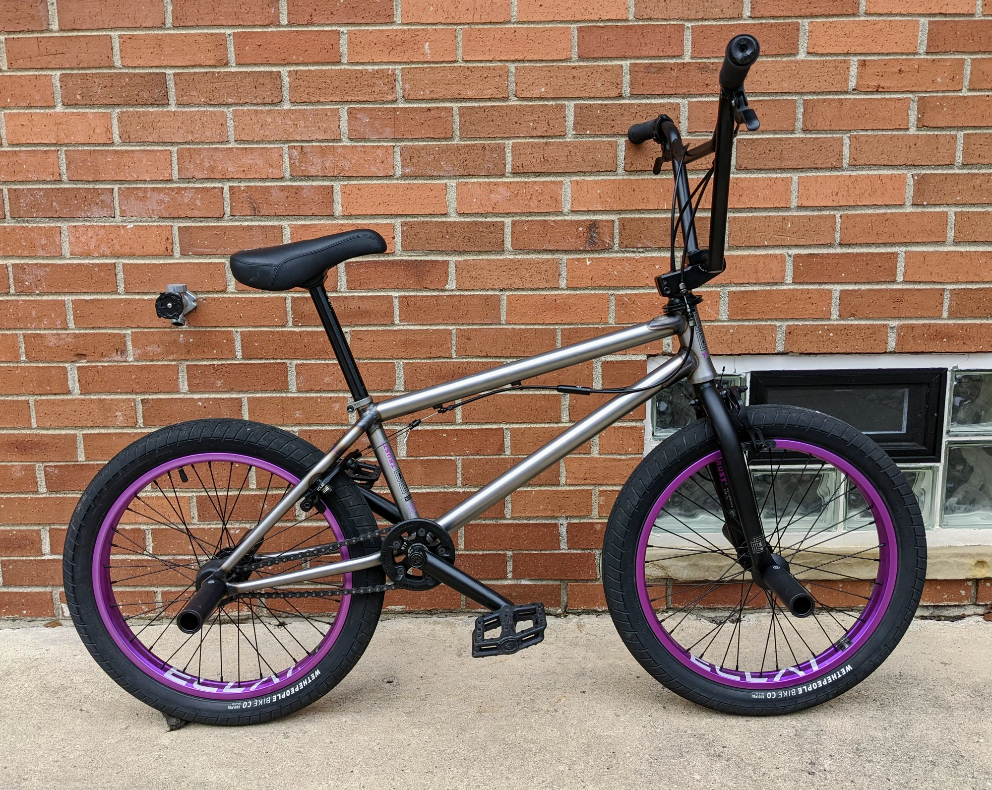 Side profile of a 2021 WTP Trust FC with a raw metal frame, black fork and components, and purple rims.